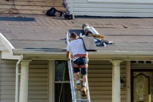A roofing inspector examines shingles and flashing on a residential roof in bright daylight.