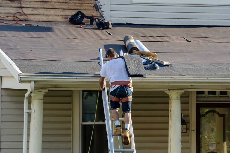 A roofing inspector examines shingles and flashing on a residential roof in bright daylight.